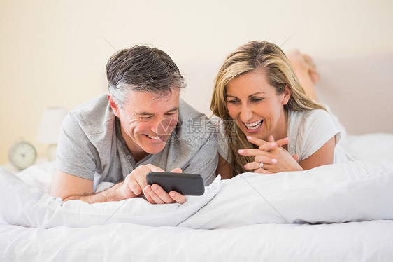 幸福的一对躺在床上看手机的情侣图片