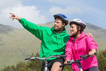 骑自行车的一对微笑的情侣穿着蒙着面的跳跃者 用男人指着图片