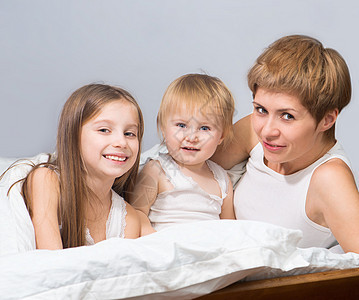 母亲和两个孩子躺在床上女性拥抱金发女郎微笑女孩卧室儿子妻子黑发母性图片