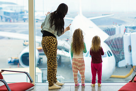 与年轻母亲在一起的小女孩在机场的大窗户上站着图片