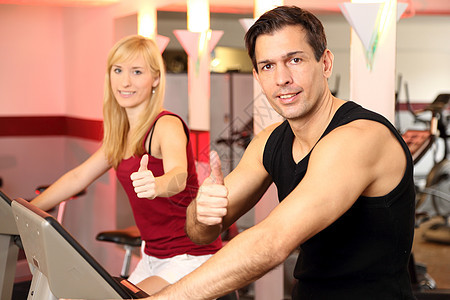 迷人的女人和男人在健身房骑自行车运动服培训师家庭教练运动机有氧运动训练健身女性运动运动装图片