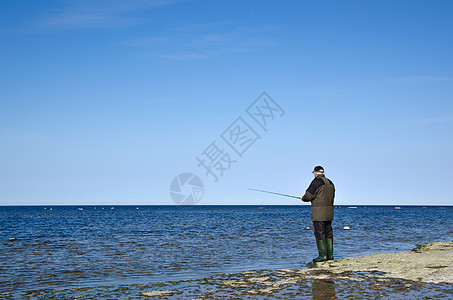 男人在平板岩石海岸捕鱼图片