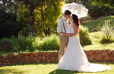 在花园婚礼上亲吻新娘和新郎面纱裙子女性树木幸福庆典女士阳伞夫妻花朵图片