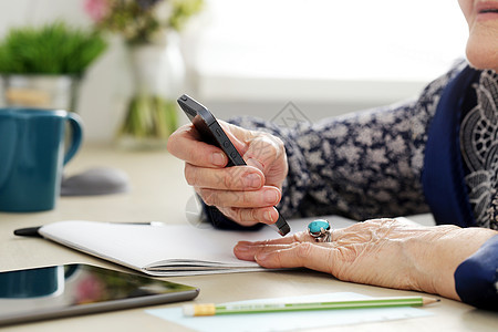 拥有移动电话的老年妇女成人女士奶奶女性桌子祖母房子触摸屏杯子戒指图片