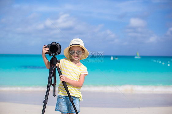 在白沙滩的三脚架上用相机拍摄小女孩的肖像图片