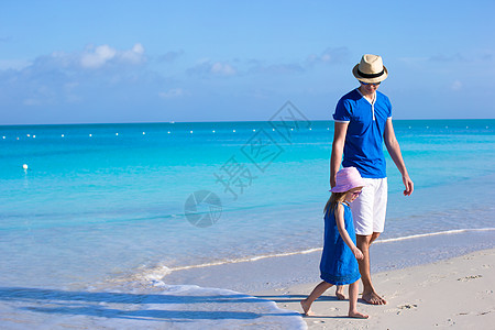 可爱的小可爱女孩和她父亲在海边走着热带父母海岸线蓝色家庭海滩异国成人女儿乐趣图片