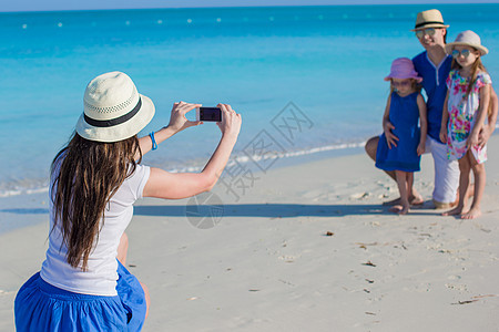 年轻母亲在海滩上用她家人的电话拍照海岸线蓝色男人摄影师父母童年假期家庭海洋快乐图片