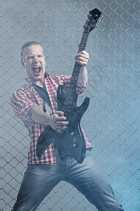 年轻音乐家 有一把吉他 在栅栏背景上演员吉他手牛仔裤旋律岩石快乐唱歌星星玩家金属图片
