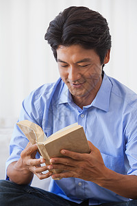 坐在沙发上看书的快乐男人衬衫牛仔布文学阅读闲暇牛仔裤男性住所家庭公寓图片