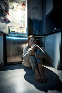 晚上在冰箱旁边吃饭的年轻女青年图片