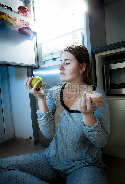 女人拿着苹果和甜甜圈对着冰箱图片