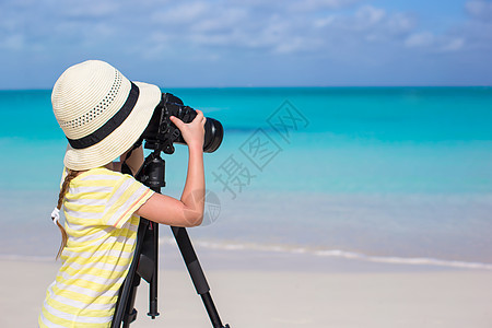 在白沙滩的三脚架上 拿着摄像机的小姑娘图片