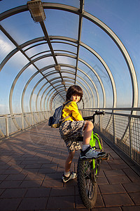 男孩骑自行车 在覆盖的桥上天桥玻璃童年孩子隧道娱乐金属闲暇男性季节图片