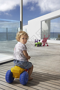 小男孩骑着玩具三轮车 在木门后视线上图片
