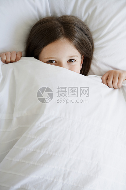 躺在床上的小女孩在脸部画像上拉盖子的高角度视野图片