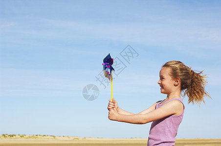 女孩站在风边的海滩上 持着针轮侧视线图片