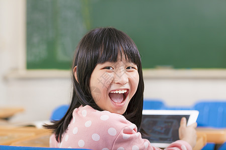 快乐的小女学生 在书桌上拿着数字平板电脑图片