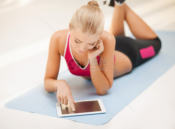 妇女用平板电脑躺在地上身体有氧运动微笑运动员女孩软垫讲师腹肌运动装健身房图片