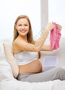 开启礼物盒的孕妇笑着微笑快乐女性新生孩子衣服母亲父母婴儿肚子开襟衫图片