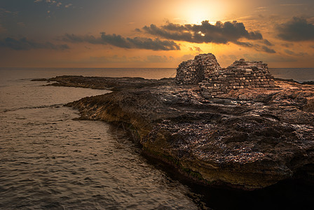 太阳用古老的废墟日落在海和洛基海岸上空地平线海洋橙子建筑学岩石海浪天空场景旅行海滩图片