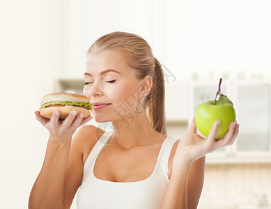 快乐的女子闻着汉堡包和拿着苹果垃圾房间营养水果厨房碳水饮食困境芝士数字图片