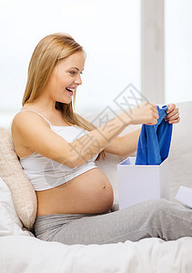 开启礼物盒的孕妇笑着微笑展示女性沙发盒子礼物说谎婴儿腹部母性新生图片