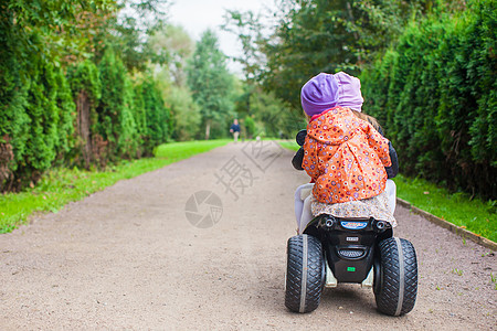 两姐妹坐在绿色公园的玩具摩托车上 坐在绿公园里婴儿快乐孩子姐姐游戏晴天裙子速度运动运输图片