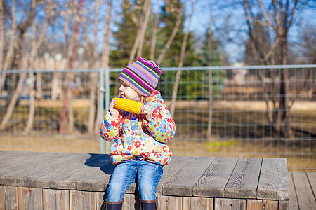 可爱的小可爱女孩 在温暖的白天在公园吃玉米女性金子植物孩子棒子烹饪小吃食物帽子粮食图片