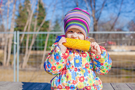 可爱的小可爱女孩 在温暖的春天天在公园吃玉米帽子烹饪童年食物女性金子种子棒子蔬菜午餐图片