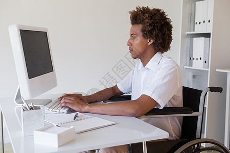 坐在轮椅上 在办公桌工作的临时重点商务人士男性商务衬衫键盘电脑机动性专注休闲残疾人屏幕图片