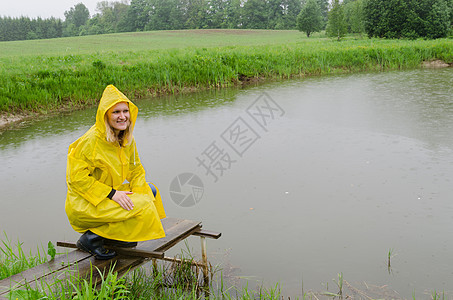 女孩在步行桥上 用黄雨衣池塘图片