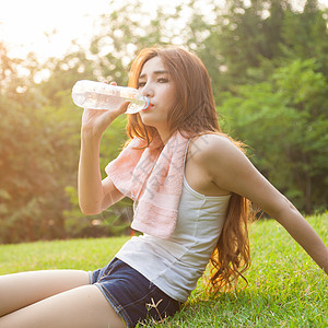 妇女在锻炼后坐着疲劳和饮用水身体女性草地毛巾成人日落女士瓶子阳光运动图片
