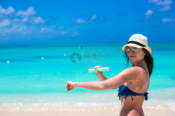 微笑的年轻女子在海滩上施晒霜女孩防晒蓝色热带海岸线异国晒黑女性棕褐色防晒霜图片