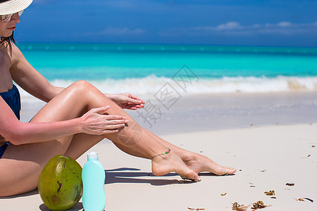 微笑的年轻女子在海滩上施晒霜游泳泳装旅行皮肤女孩太阳镜系数海洋热带女性图片