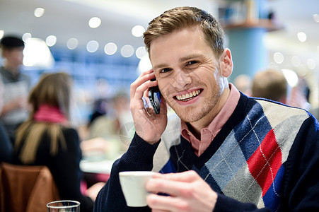在咖啡馆使用移动电话的青年男子咖啡男性细胞微笑桌子冒充毛衣技术男人餐厅图片