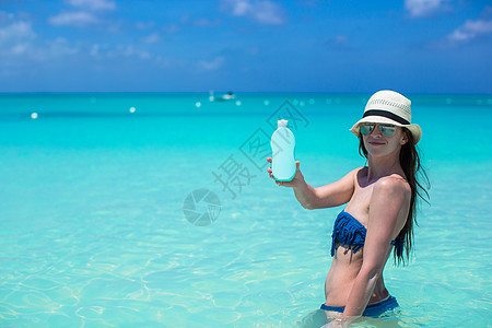 在热带沙滩上用防晒霜微笑的年轻女子图片