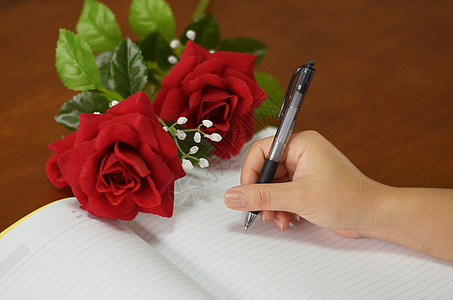 手握笔笔笔 用玫瑰写在笔记本上桌子商业女性圆珠笔记事本日记人手写作水平空白图片