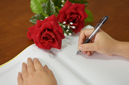 手握笔笔笔 用玫瑰写在笔记本上日记人手写作女性记事本商业圆珠笔桌子水平空白图片