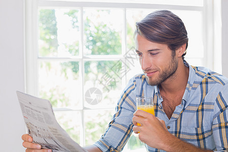 边看报纸边喝橘子汁的笑脸男子家庭生活男性家庭住所阅读桌子公寓衬衫空余微笑背景图片