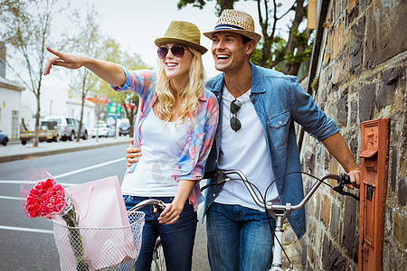 一对小情侣骑着自行车站在砖墙旁边快乐潮人女性男人闲暇手势微笑感情城市生活活动图片
