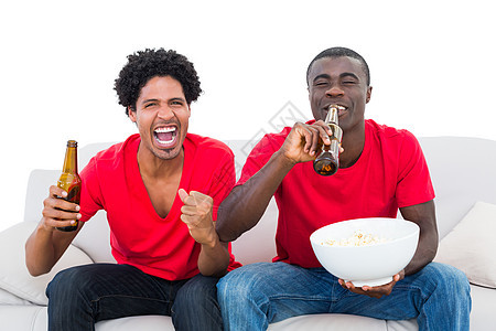 用啤酒和爆米花在沙发上欢呼的红足球球迷杯子观众男性微笑快乐朋友支持者拳头活力扇子图片