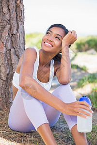 坐在树上装水瓶子的合适妇女运动水壶阳光农村环境混血女士身体晴天运动服图片