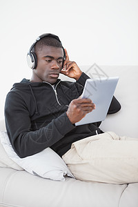 坐在沙发上听平板电脑音乐的无所事事的人黑色休闲住所服装家庭生活触摸屏男人家庭耳机房子图片