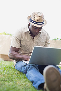 英俊男人用笔记本电脑在花园里放松毡帽帽子黑色服装技术闲暇休闲衬衫男性家庭生活图片