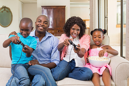在沙发上玩电子游戏的快乐家庭放松感情女士闲暇父亲控制器房子视频儿子家庭生活长椅图片