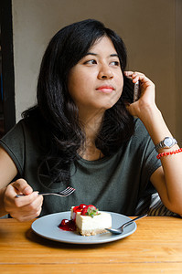 年轻女孩在咖啡厅里讲手机和蛋糕图片
