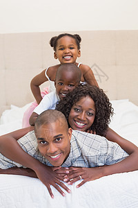 幸福的一家人一起在床上对着相机微笑女儿乐趣羽绒被坐垫父亲男生童年家庭生活卧室女士图片