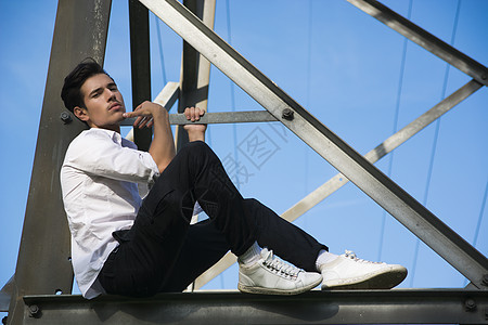 坐在金属电塔上的英俊年轻男子;图片