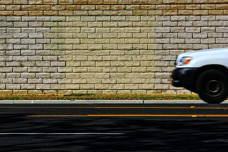 有砖墙背景的白色汽车在路上行驶背景图片