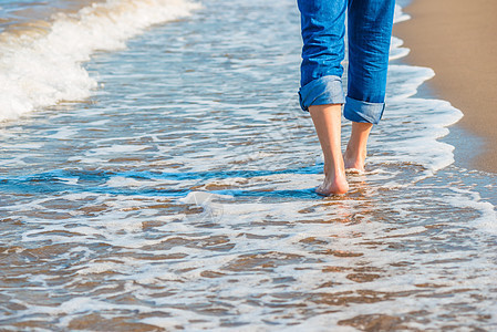 穿着牛仔裤的男性大腿沿沙海滨行走图片